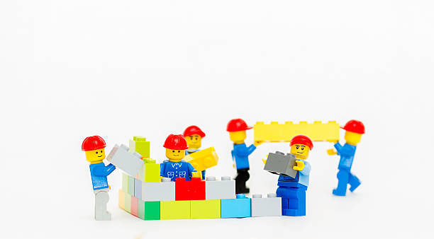 Figurines LEGO ouvriers en casques rouges et tenues bleues construisant un mur coloré avec des briques de construction