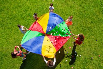 Vue de dessus d'enfants se tenant en cercle sur la pelouse verte et tenant un parachute arc-en-ciel rempli de balles colorées.
